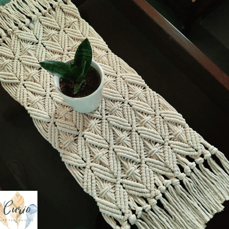macrame table runner laid on a table and a planter placed on top of the macrame runner