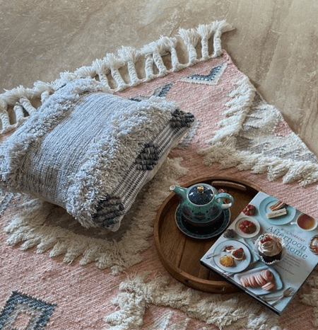 a grey hand woven cushion placed over a pink kilim vintage rug for boho effect